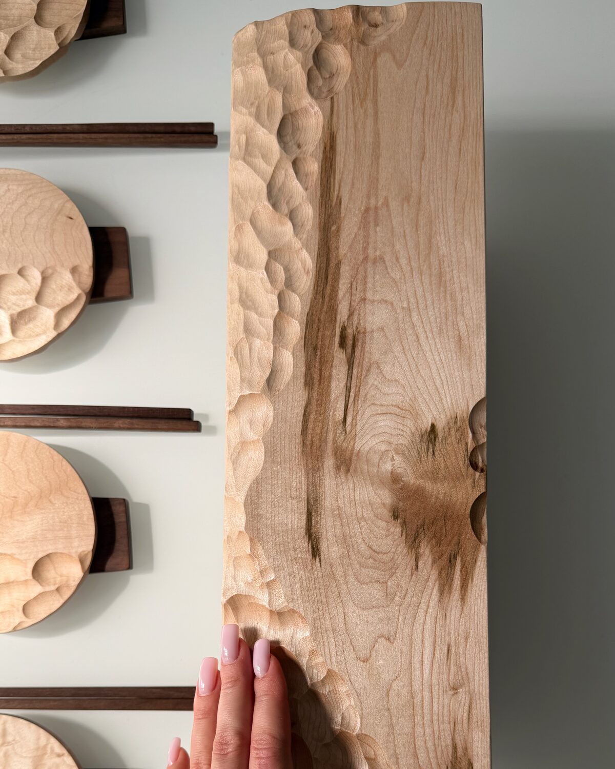 A hand resting on the wave-carved maple board, showing its scale