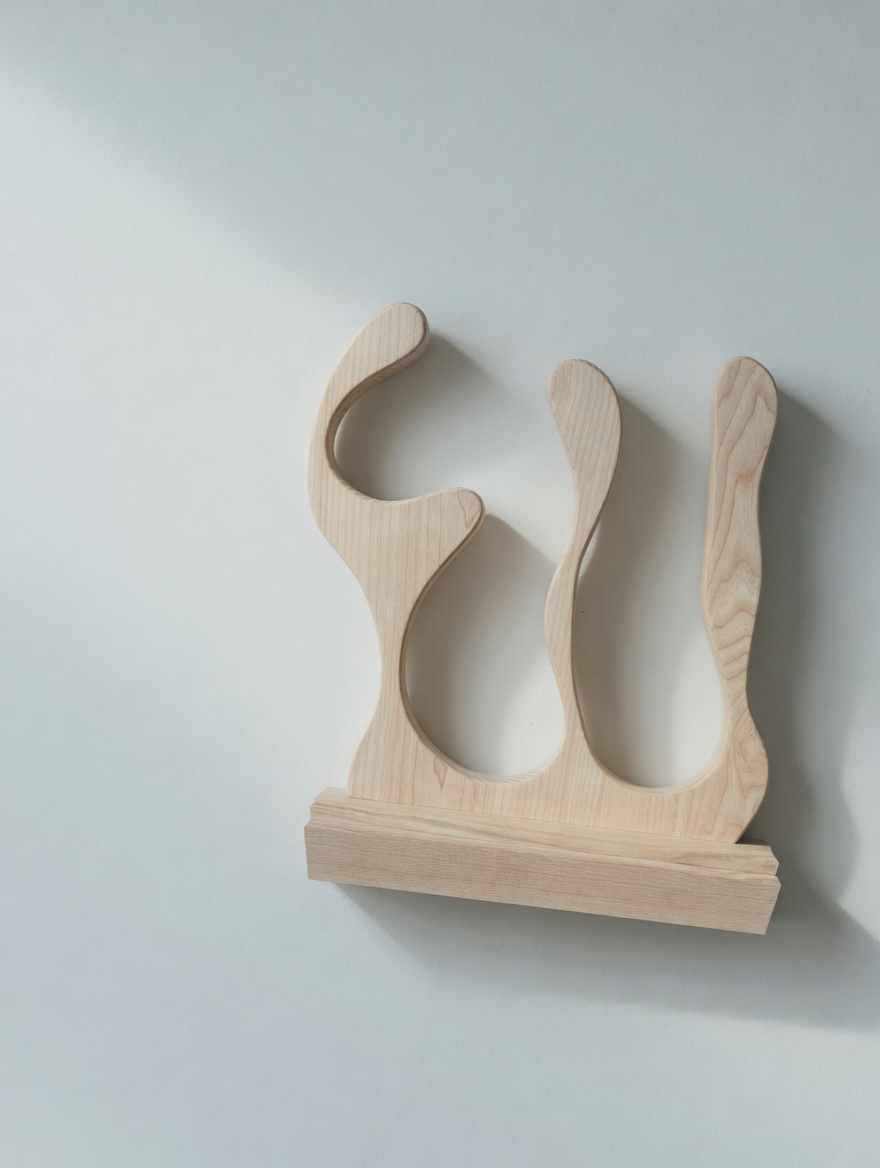 An ash sculpture, three flowing forms on a slim base, against a soft wall